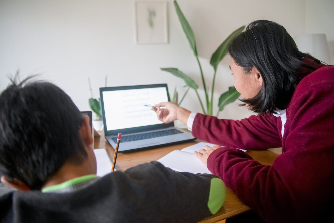 Adult guiding child in learning session using a laptop at home. Ideal for education themes.